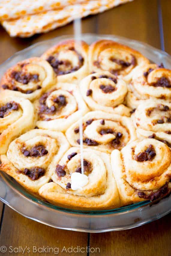 drizzling icing onto banana chocolate chip cinnamon rolls in a glass baking dish