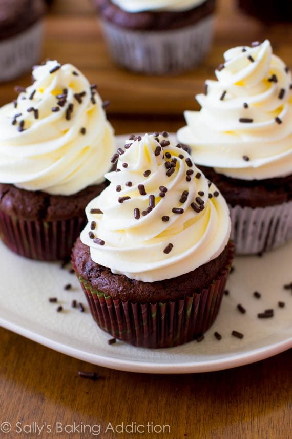 chocolate cupcakes topped with white chocolate frosting and chocolate sprinkles on a white plate