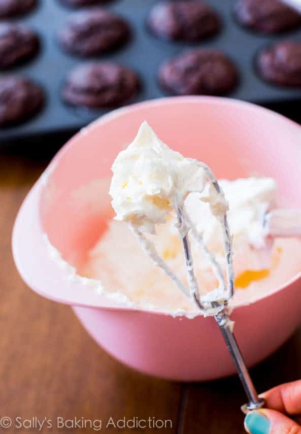 white chocolate frosting in a pink bowl with hand mixer beaters