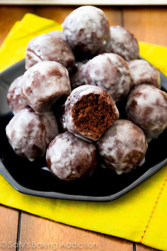 stack of glazed chocolate donut holes with a bite taken from one on a black plate