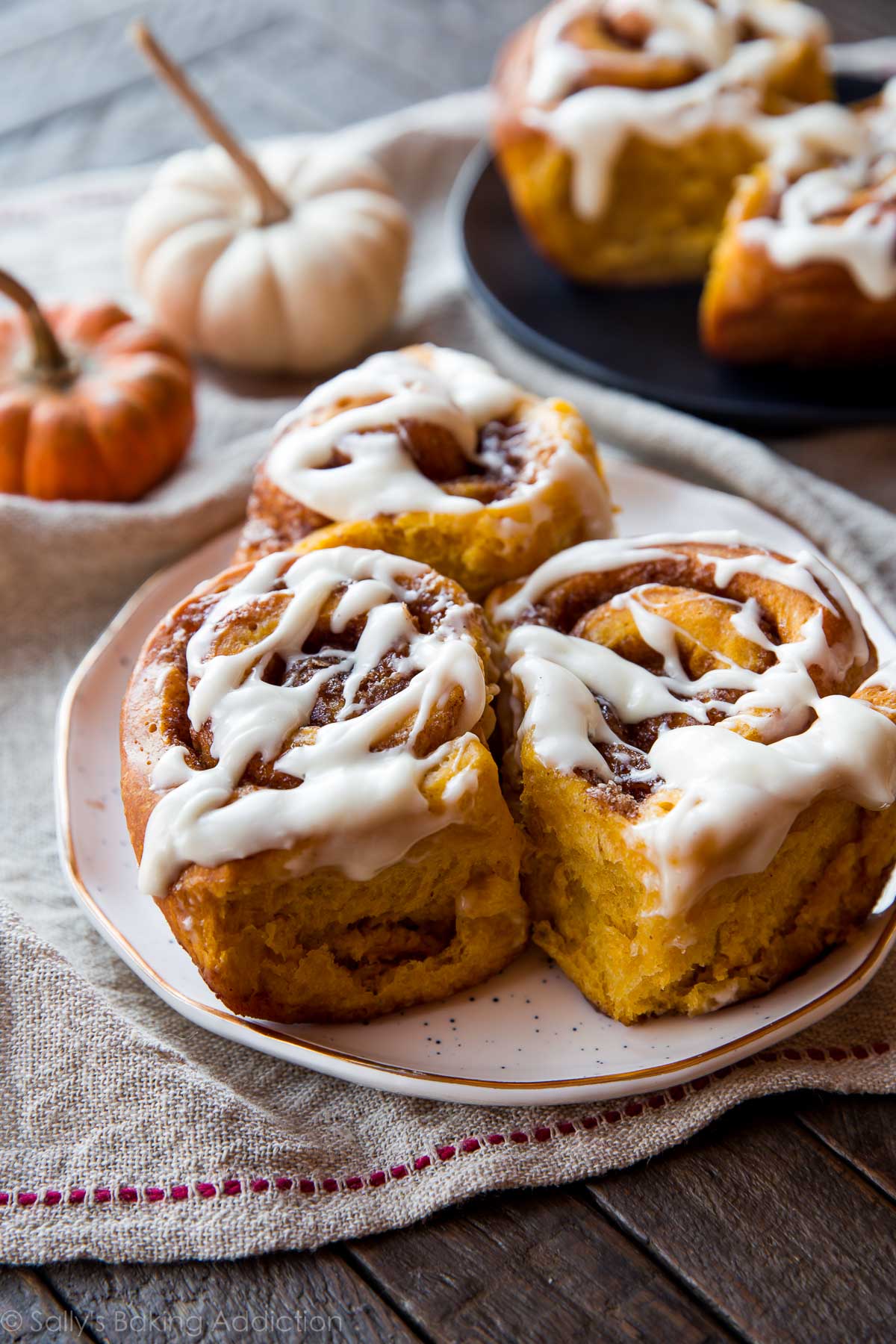 pumpkin cinnamon rolls with maple cream cheese icing on a white plate