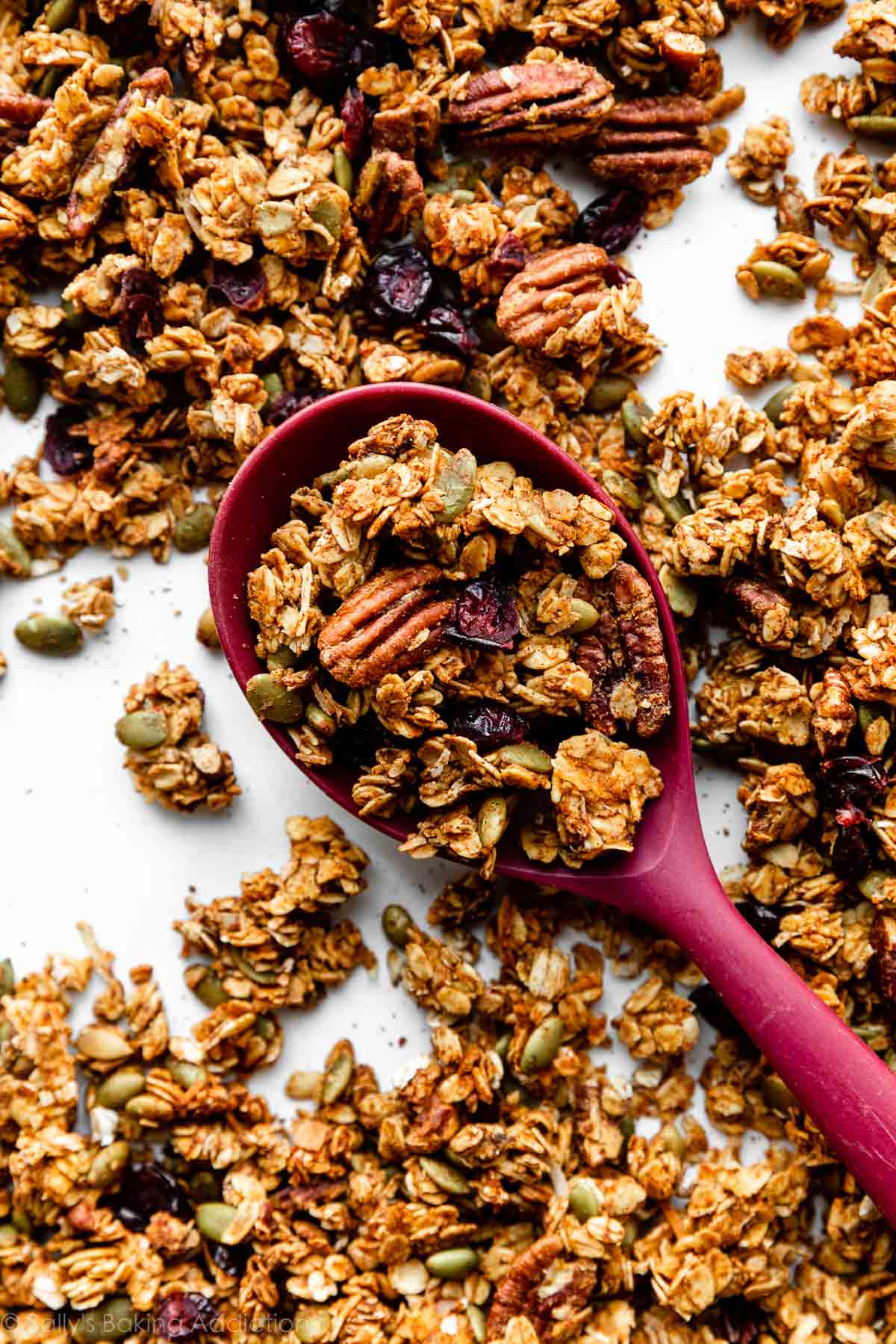 pink spoon picking up pumpkin granola filled with pecans, dried cranberries, and pepitas.