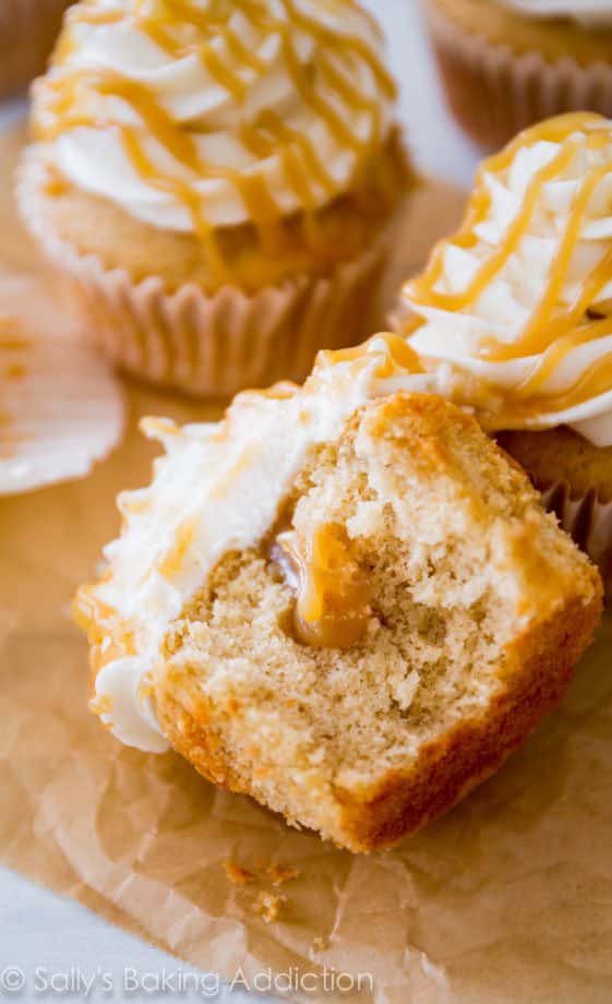 brown sugar cupcakes topped with vanilla frosting and butterscotch drizzle with one cut in half showing the inside