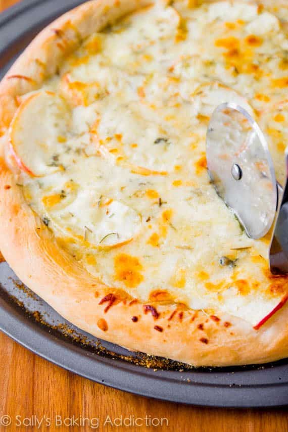 caramelized apple gorgonzola pizza on a pizza pan with a pizza cutter