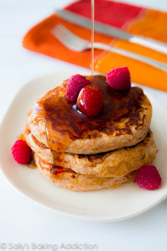 stack of whole wheat oatmeal pancakes topped with raspberries and maple syrup on a white plate