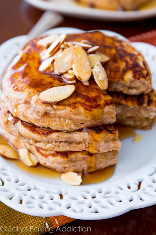 stack of whole wheat oatmeal pancakes topped with slivered almonds and maple syrup on a white plate