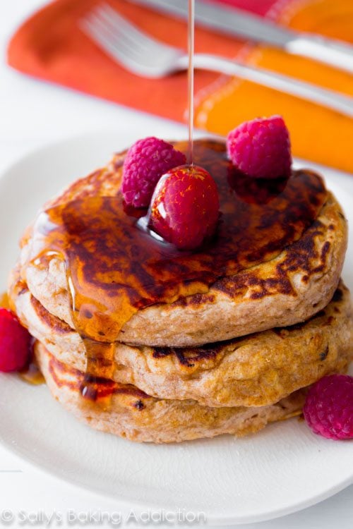 stack of whole wheat oatmeal pancakes topped with raspberries and maple syrup on a white plate