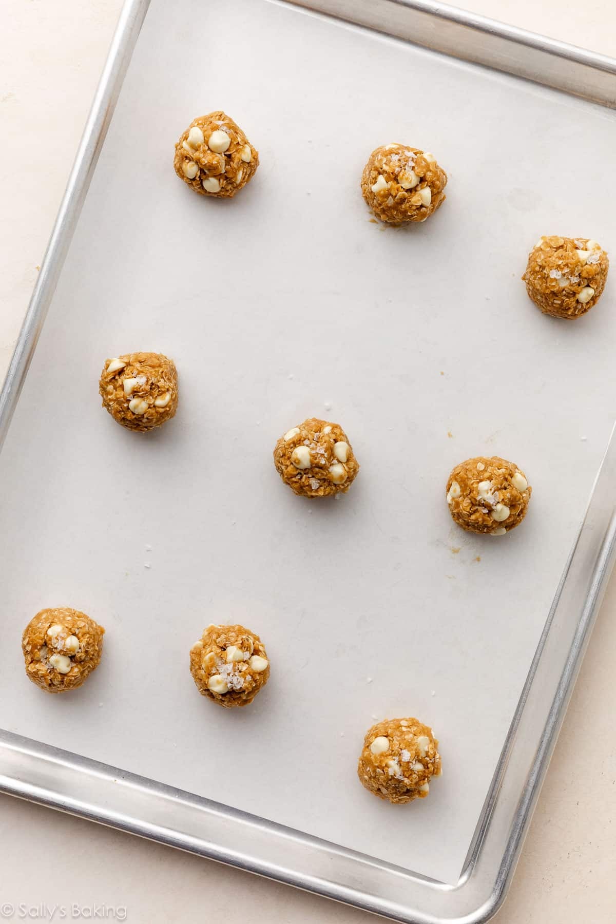 9 cookie dough balls on a lined baking sheet topped with sea salt flakes.
