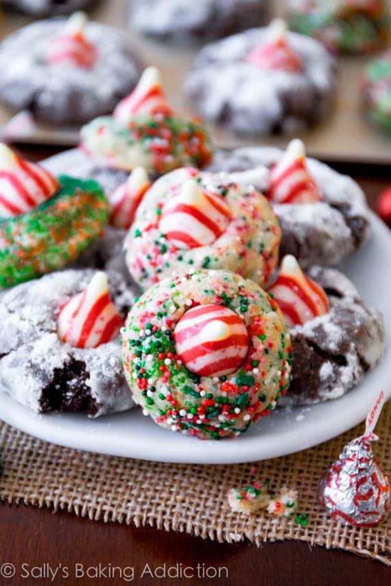 sugar cookies and chocolate cookies with christmas sprinkles with a candy cane Hershey's kiss on top on a white plate