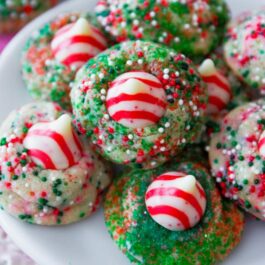 sugar cookies with christmas sprinkles with a candy cane Hershey's kiss on top on a white plate