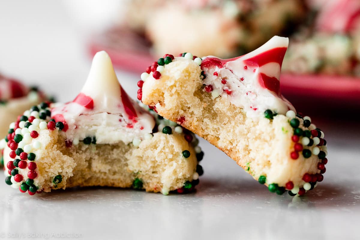 two candy cane kiss sugar cookies rolled in sprinkles with bites taken out.