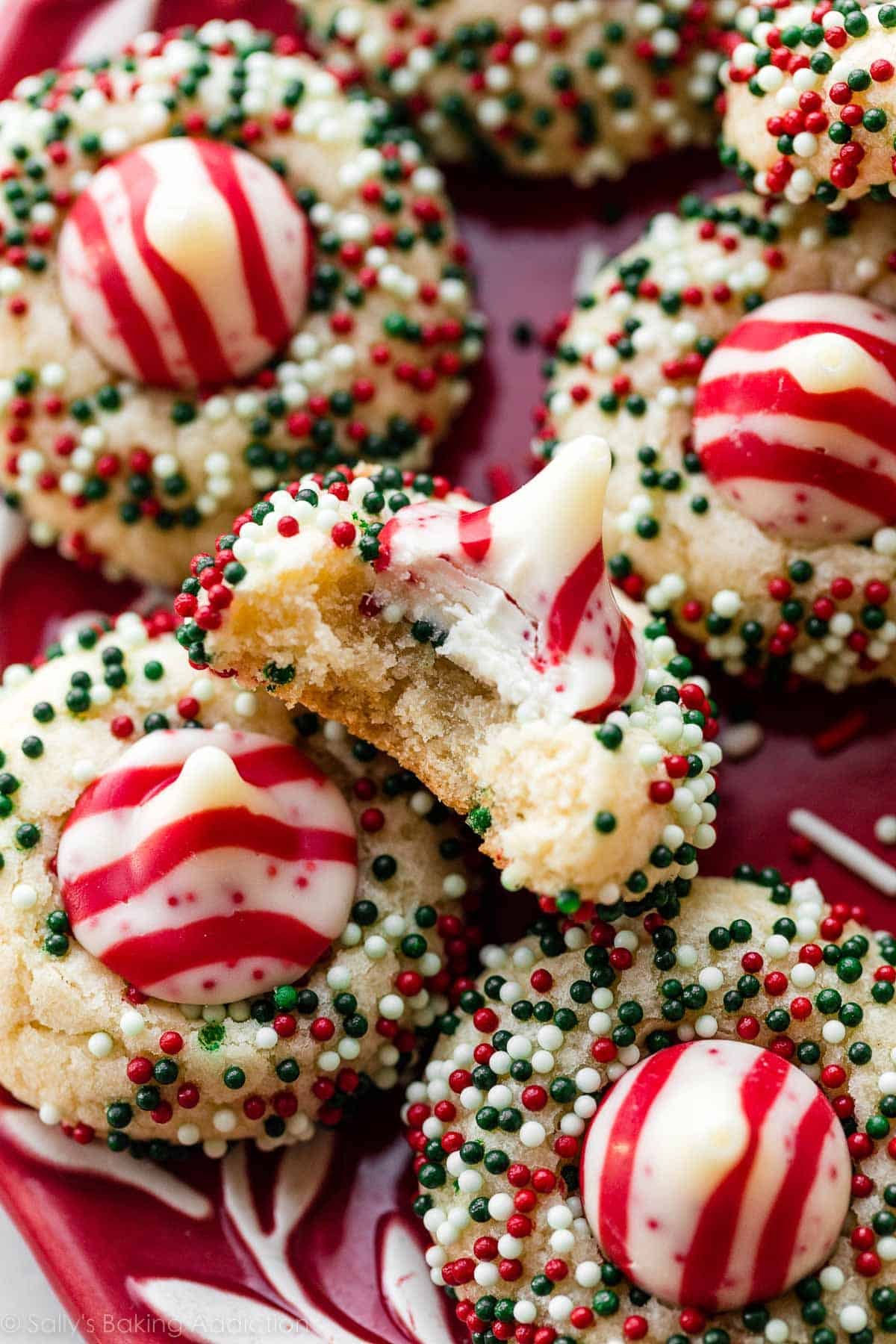 candy cane kiss cookies rolled in nonpareil sprinkles and one cookie with bite taken out.