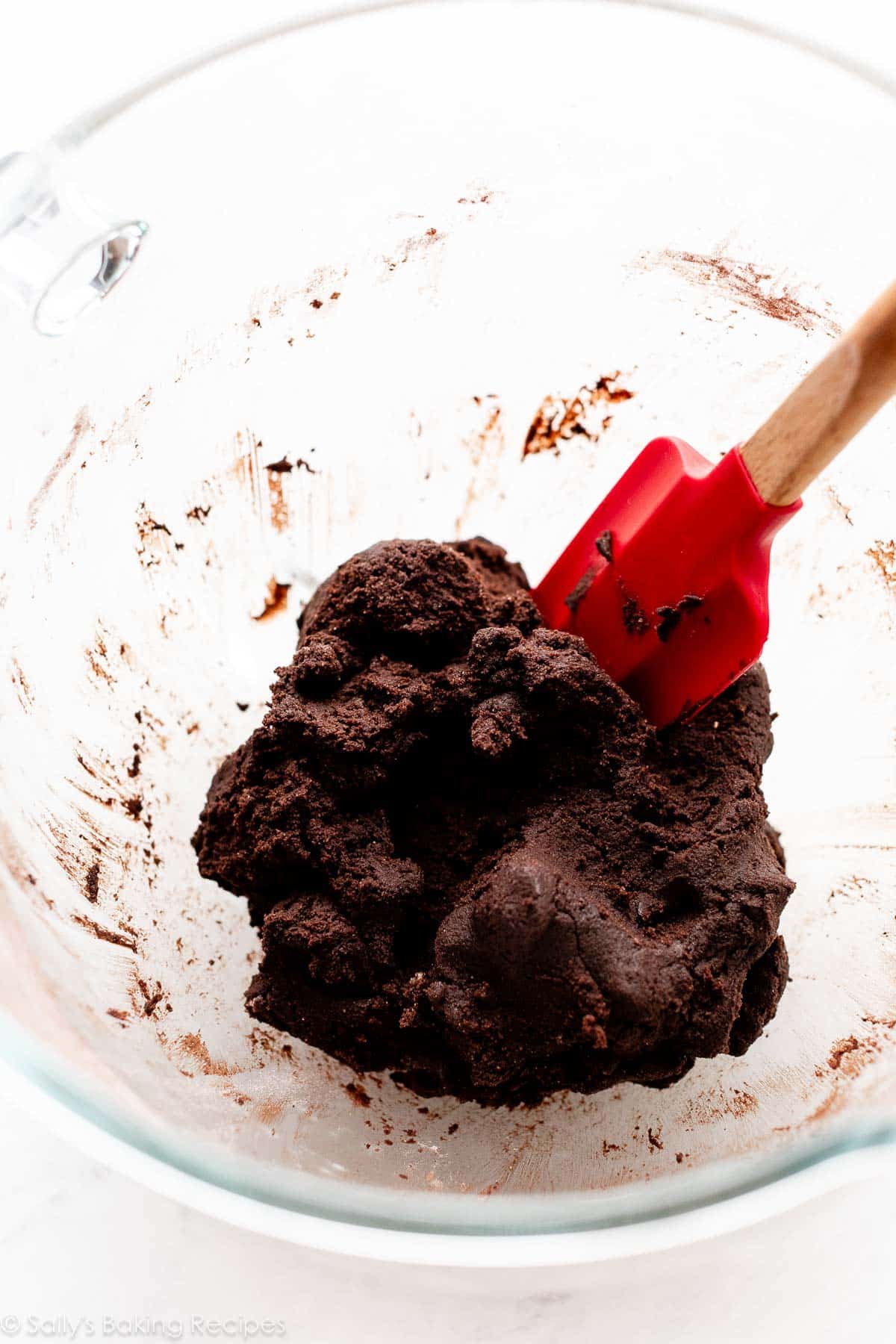 dark cocoa cookie dough in glass bowl with red spatula.