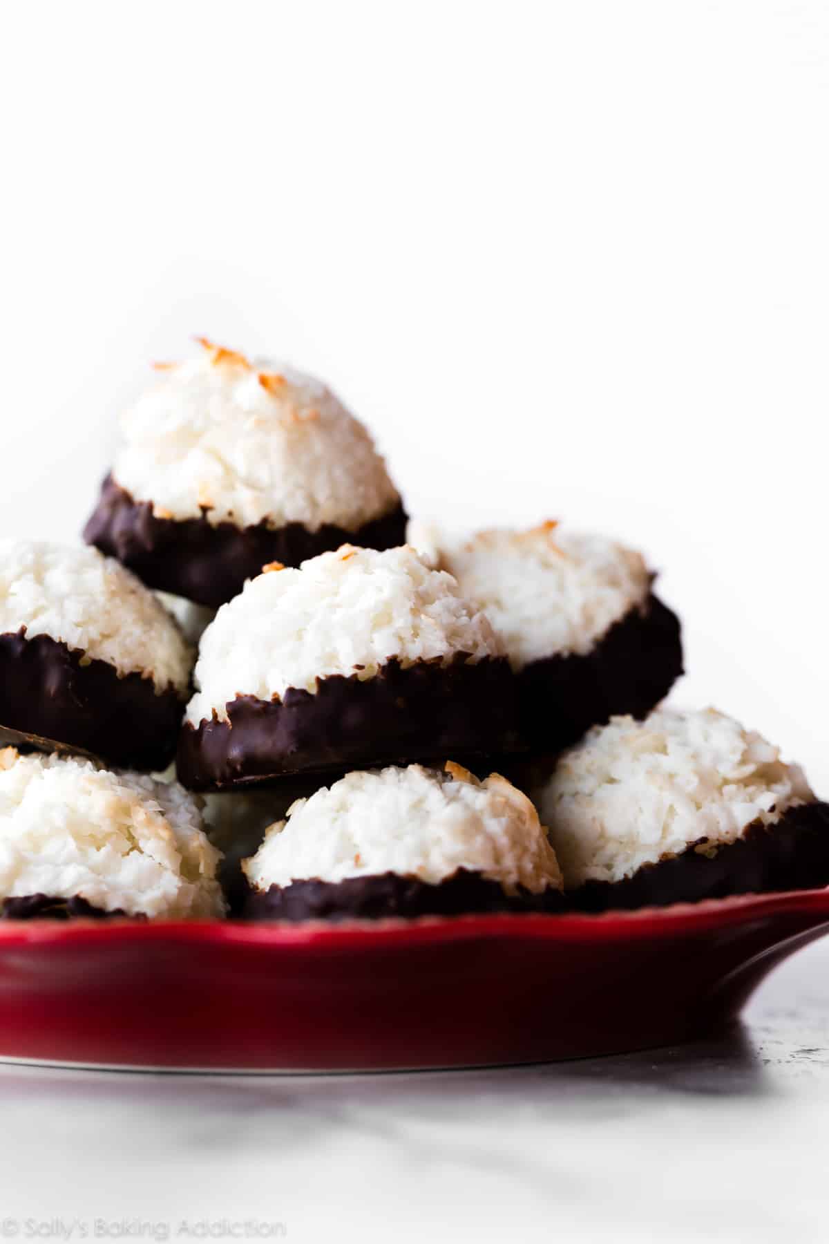 stack of coconut macaroons dipped in dark chocolate on a red plate