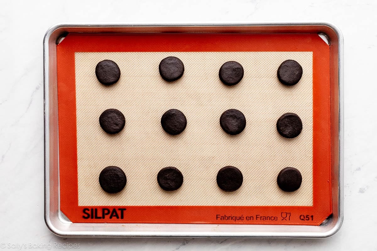 12 flattened cookie dough balls on Silpat-lined baking sheet.