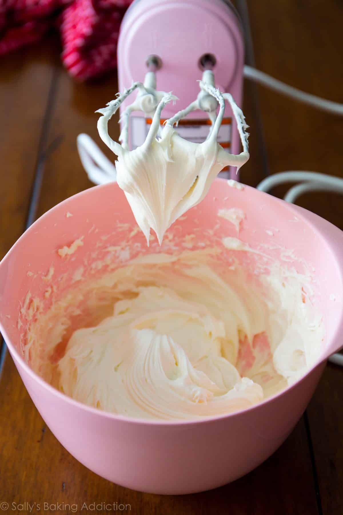 cream cheese frosting in a pink bowl with a hand mixer