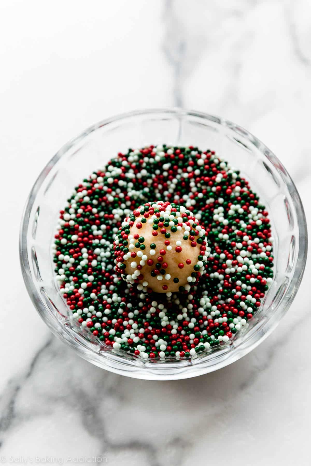 rolling a cookie dough ball in white, red, and green nonpareil sprinkles.