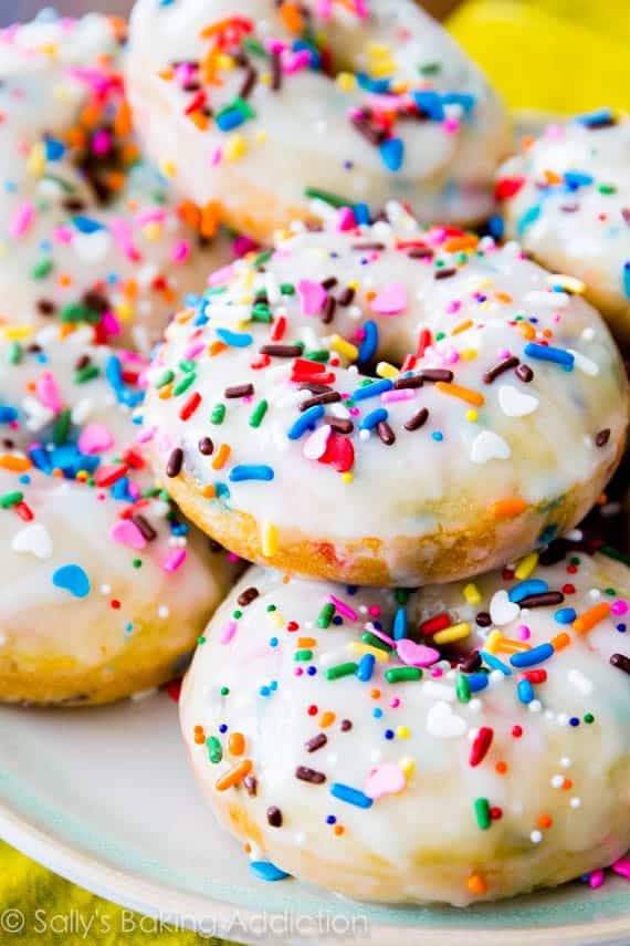 pile of baked funfetti donuts topped with vanilla glaze and sprinkles on a white plate