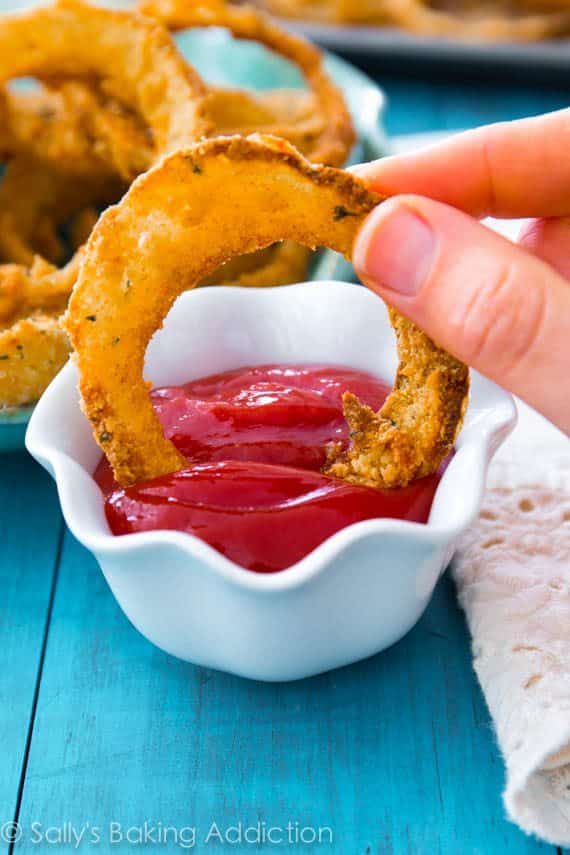 hand dipping onion ring into bowl of ketchup