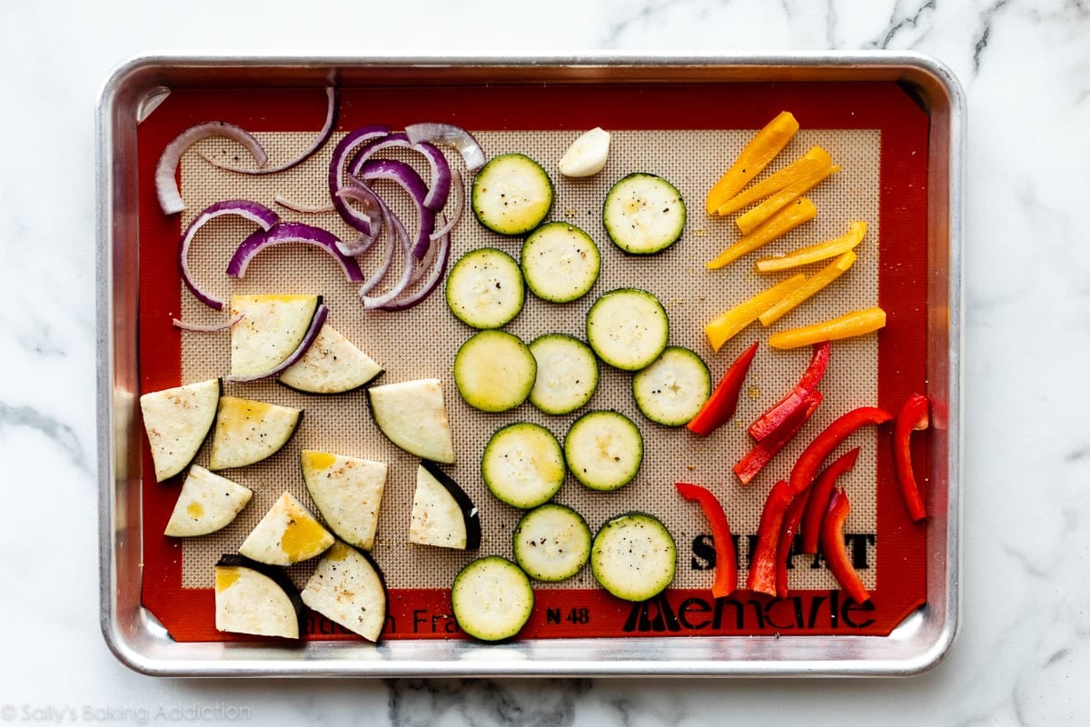 vegetables on lined baking sheet including eggplant, red pepper, yellow pepper, red onion, and zucchini