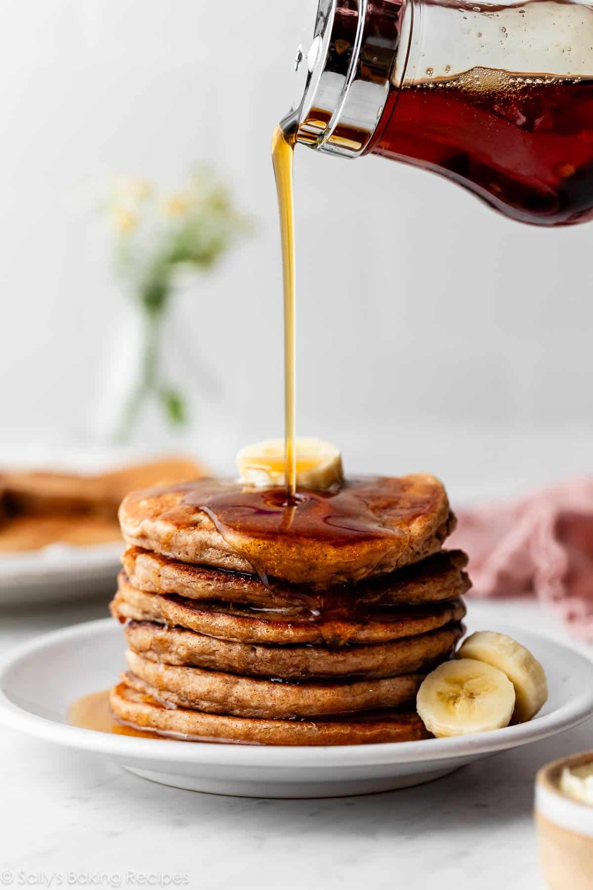 stack of healthy whole wheat banana pancakes with maple syrup being poured on top.