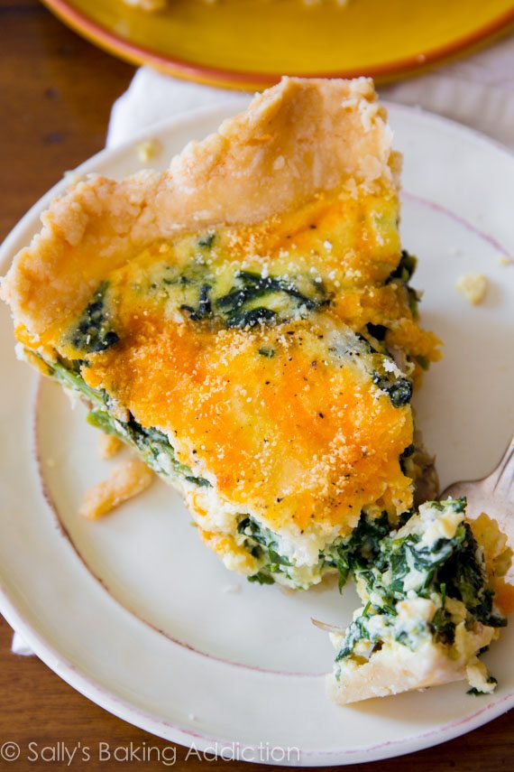 slice of cheese spinach quiche on a white plate with a fork