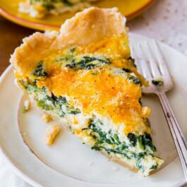 slice of cheesy spinach quiche on a white plate with a fork