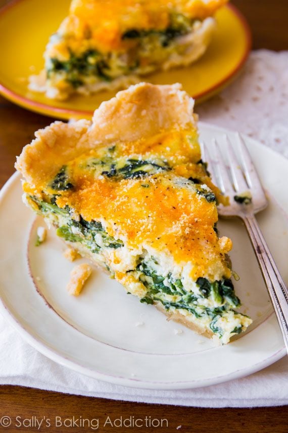 slice of cheesy spinach quiche on a white plate with a fork