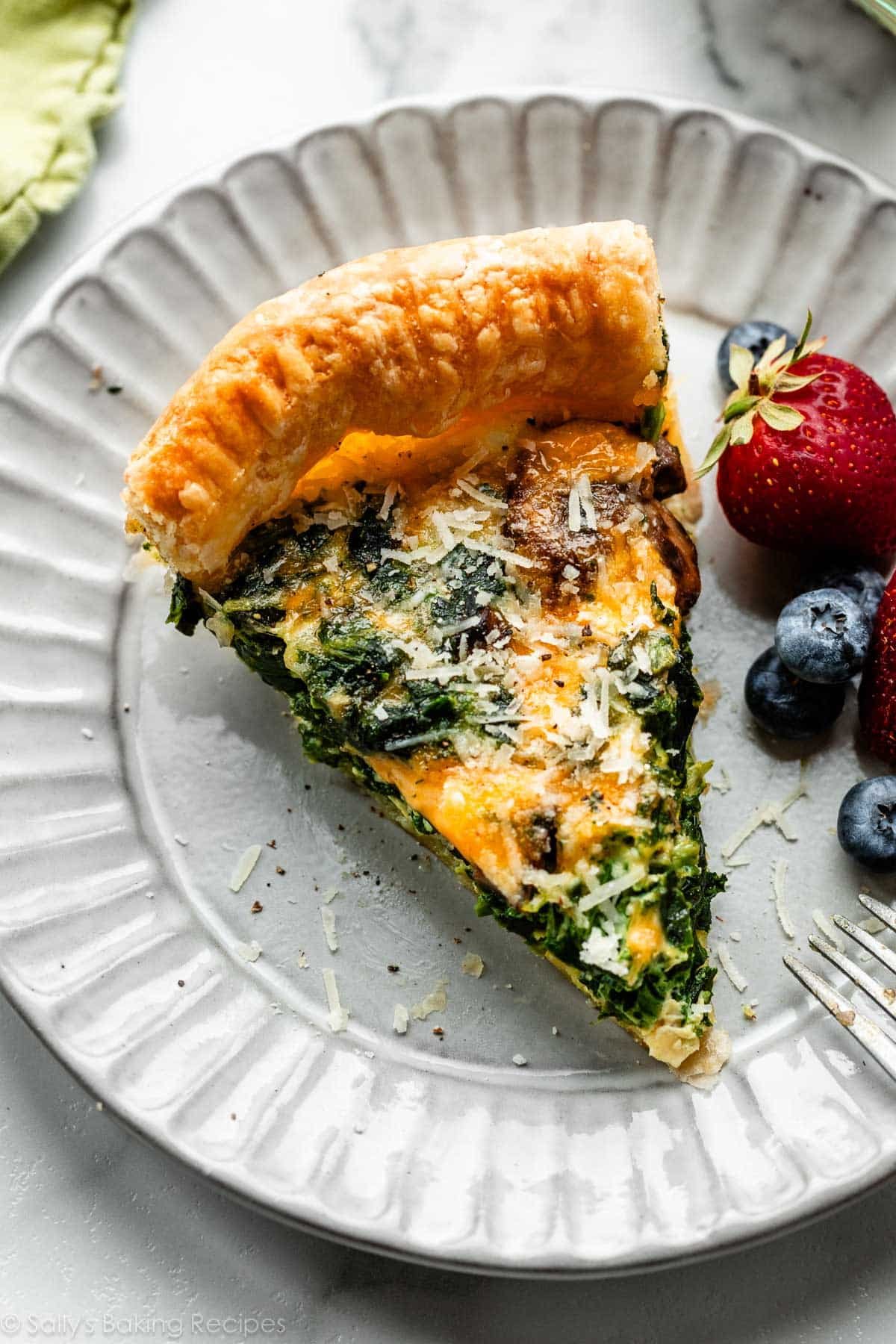 slice of cheesy spinach quiche on gray plate with fresh berries.
