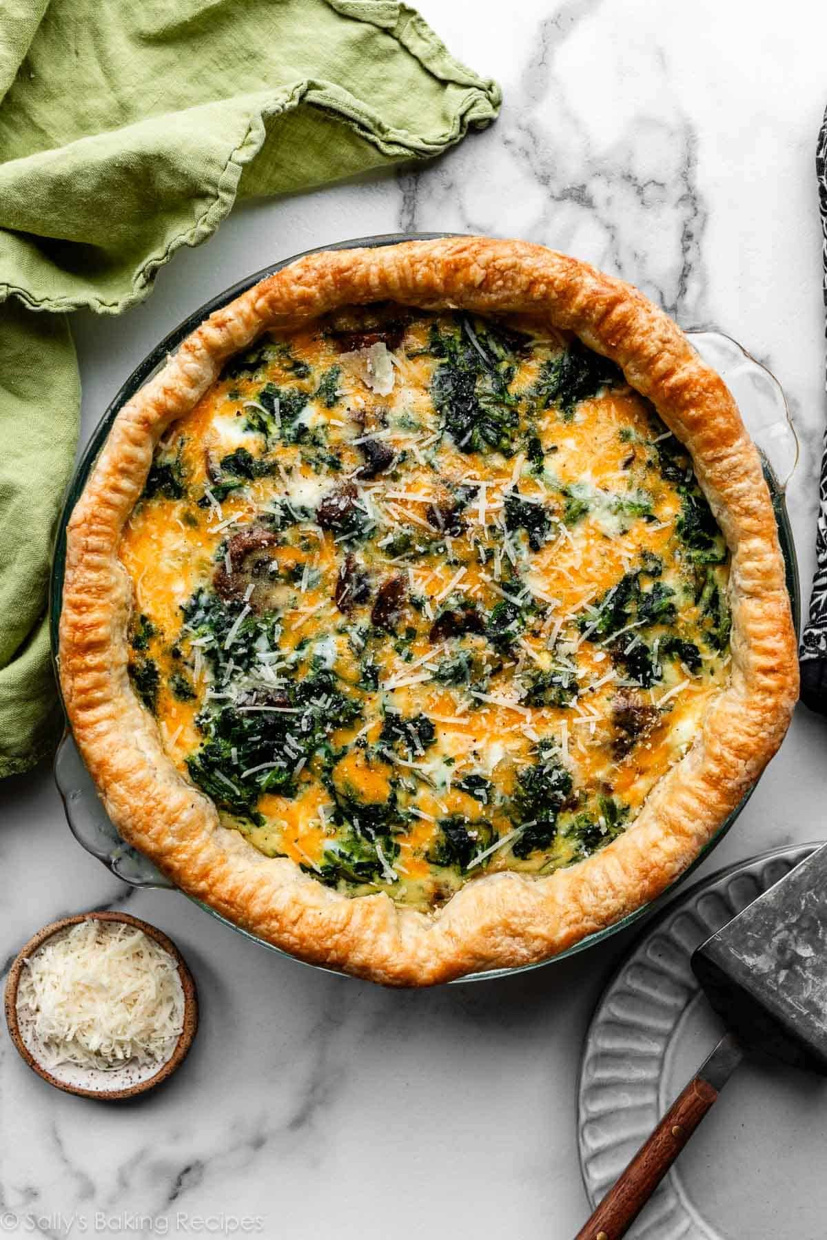 cheesy spinach quiche in pie crust with fresh parmesan cheese sprinkled on top.