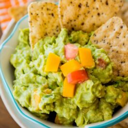 mango guacamole in a white bowl with chips on a plate