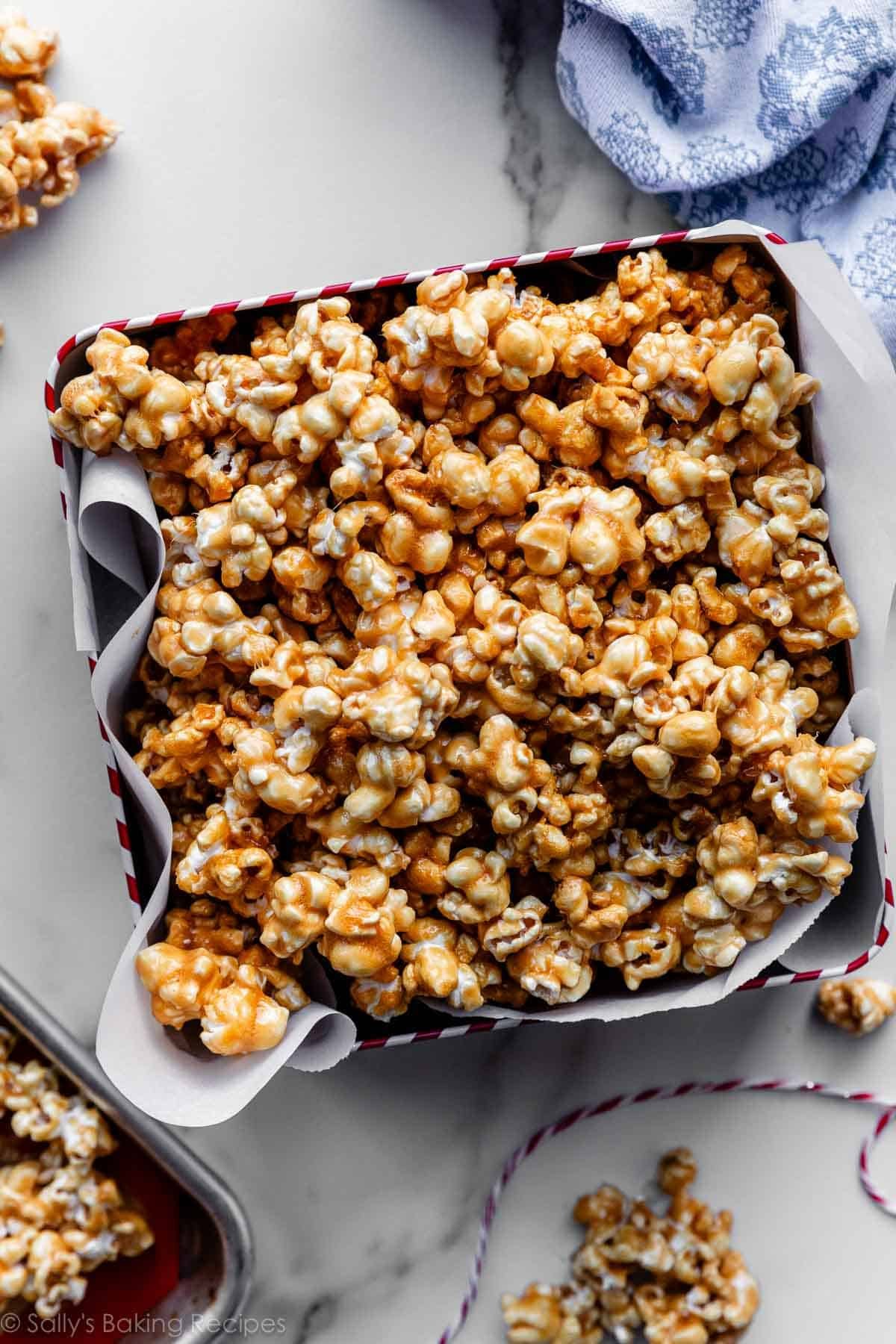 homemade caramel corn popcorn in tin with blue linen and caramel corn scattered around it.