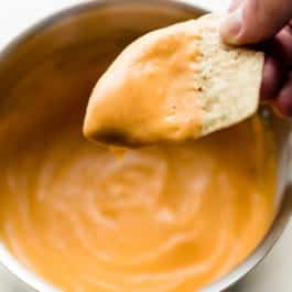 dipping a chip into bowl of nacho cheese sauce