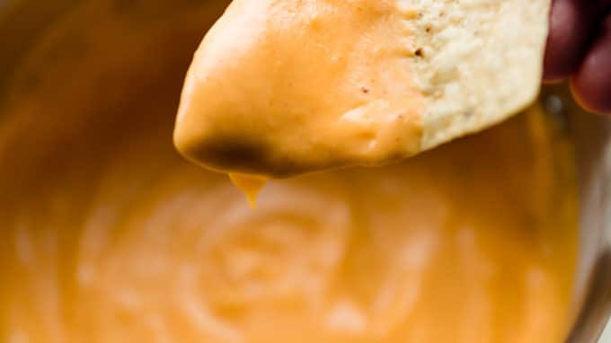 dipping a chip into bowl of nacho cheese sauce