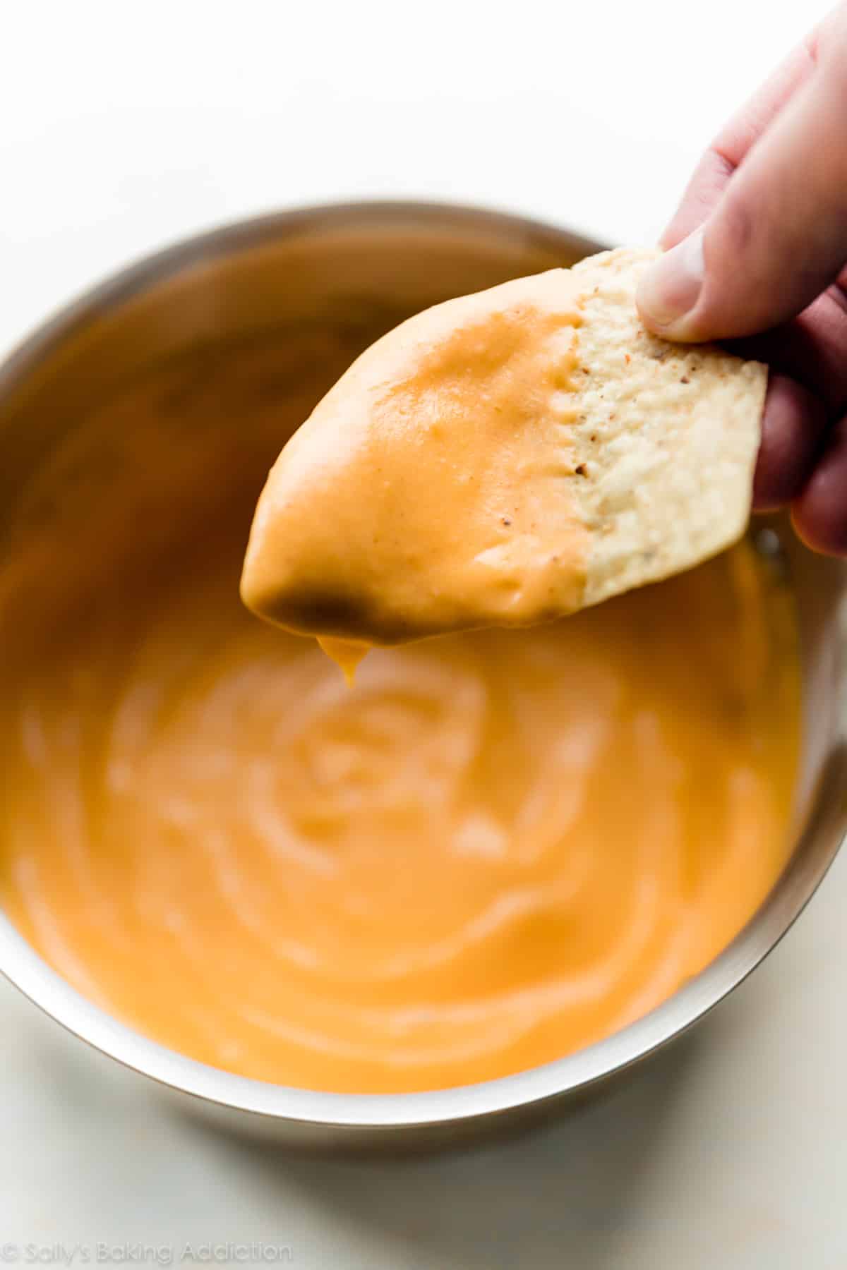 dipping a chip into bowl of nacho cheese sauce