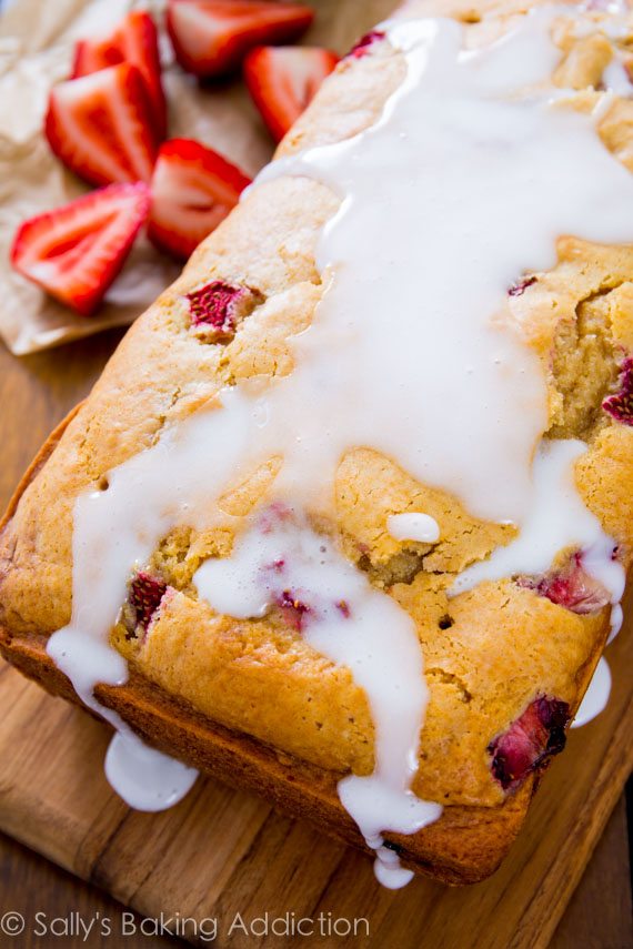 loaf of glazed strawberry bread with vanilla icing on a wood board