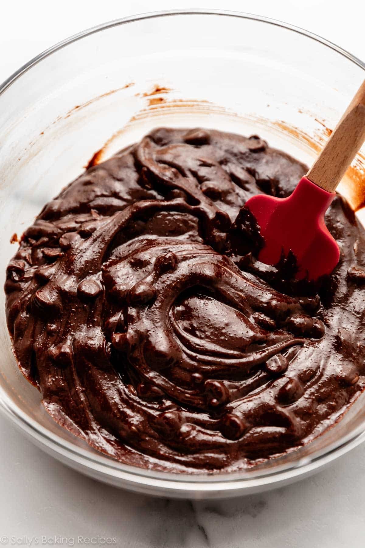 chocolate batter with chocolate chips in glass bowl with red spatula.