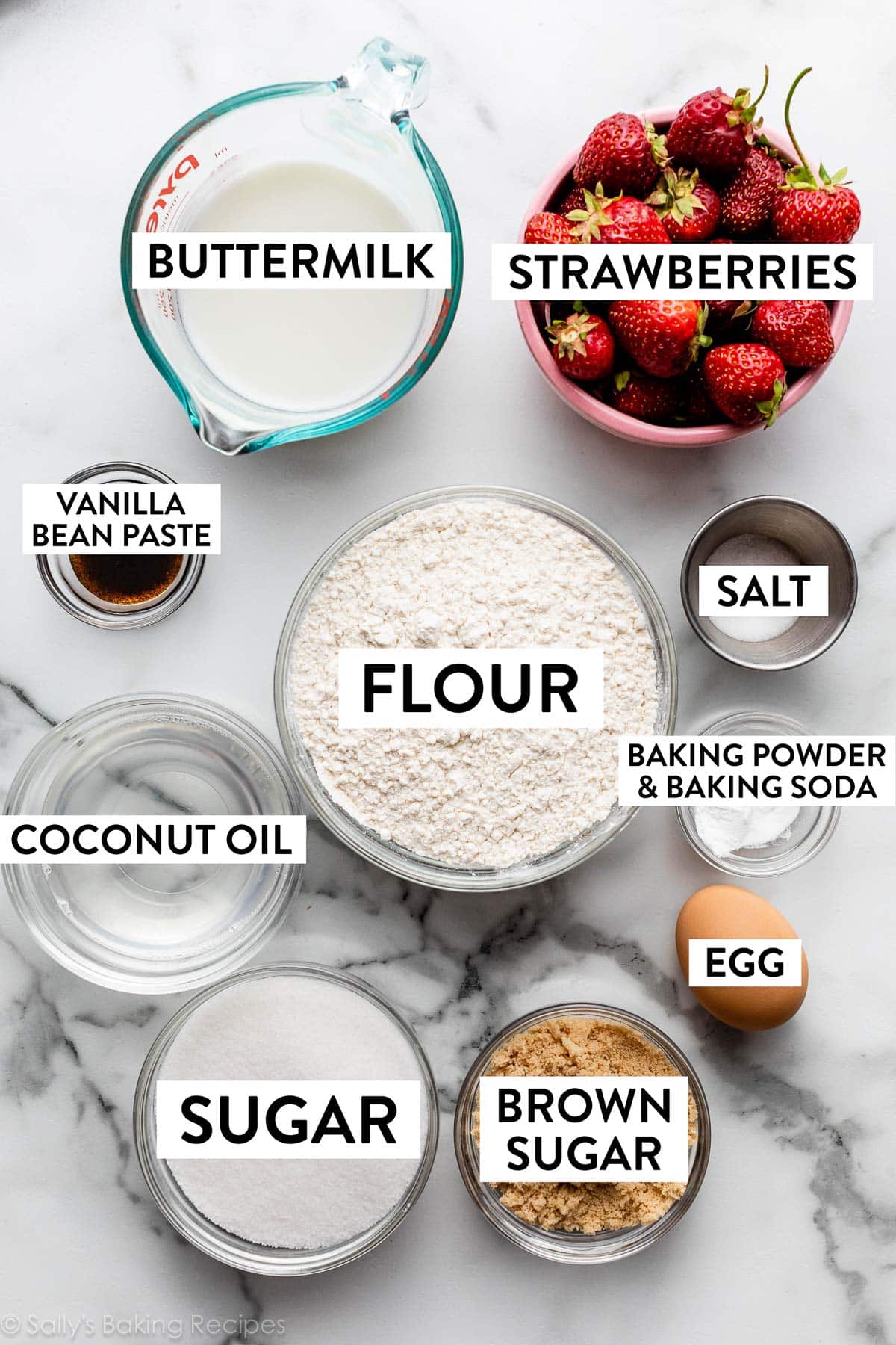 ingredients in bowls on counter including strawberries, buttermilk, flour, egg, brown sugar, sugar, melted coconut oil, and vanilla bean paste.
