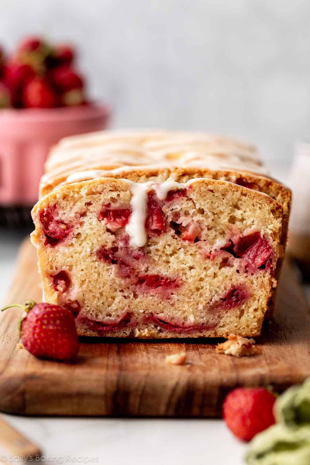 strawberry bread with lots of strawberries inside and vanilla glaze on top sitting on cutting board.