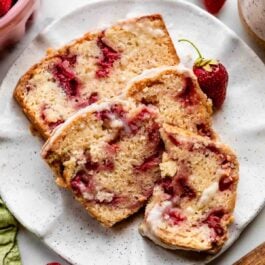 strawberry bread slices on white speckled plate with strawberries around it.