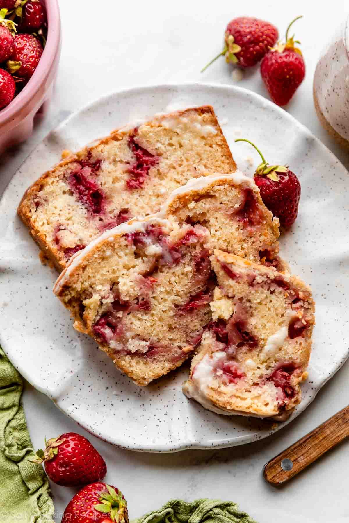 strawberry bread slices on white speckled plate with strawberries around it.