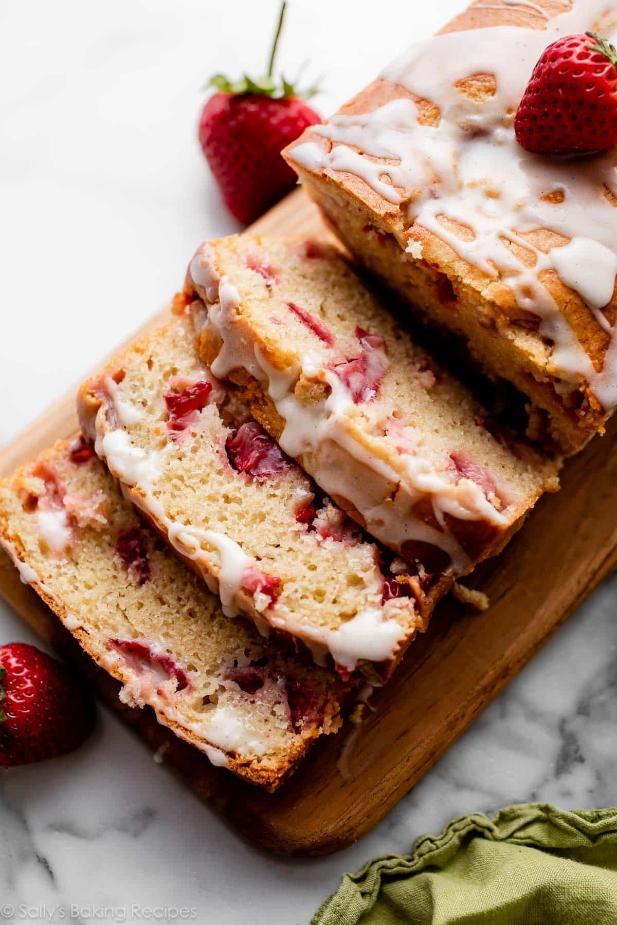 sliced and glazed strawberry bread with lots of strawberries inside sitting on cutting board.