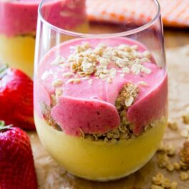 layers of strawberry smoothie, mango smoothie, and granola in a glass