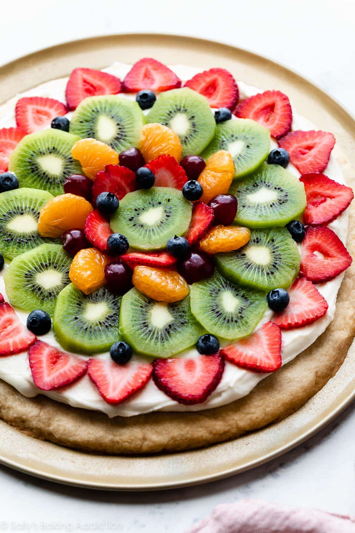 decorated sugar cookie fruit pizza on pizza pan with strawberries, kiwi, blueberries, grapes, and mandarin oranges on top.