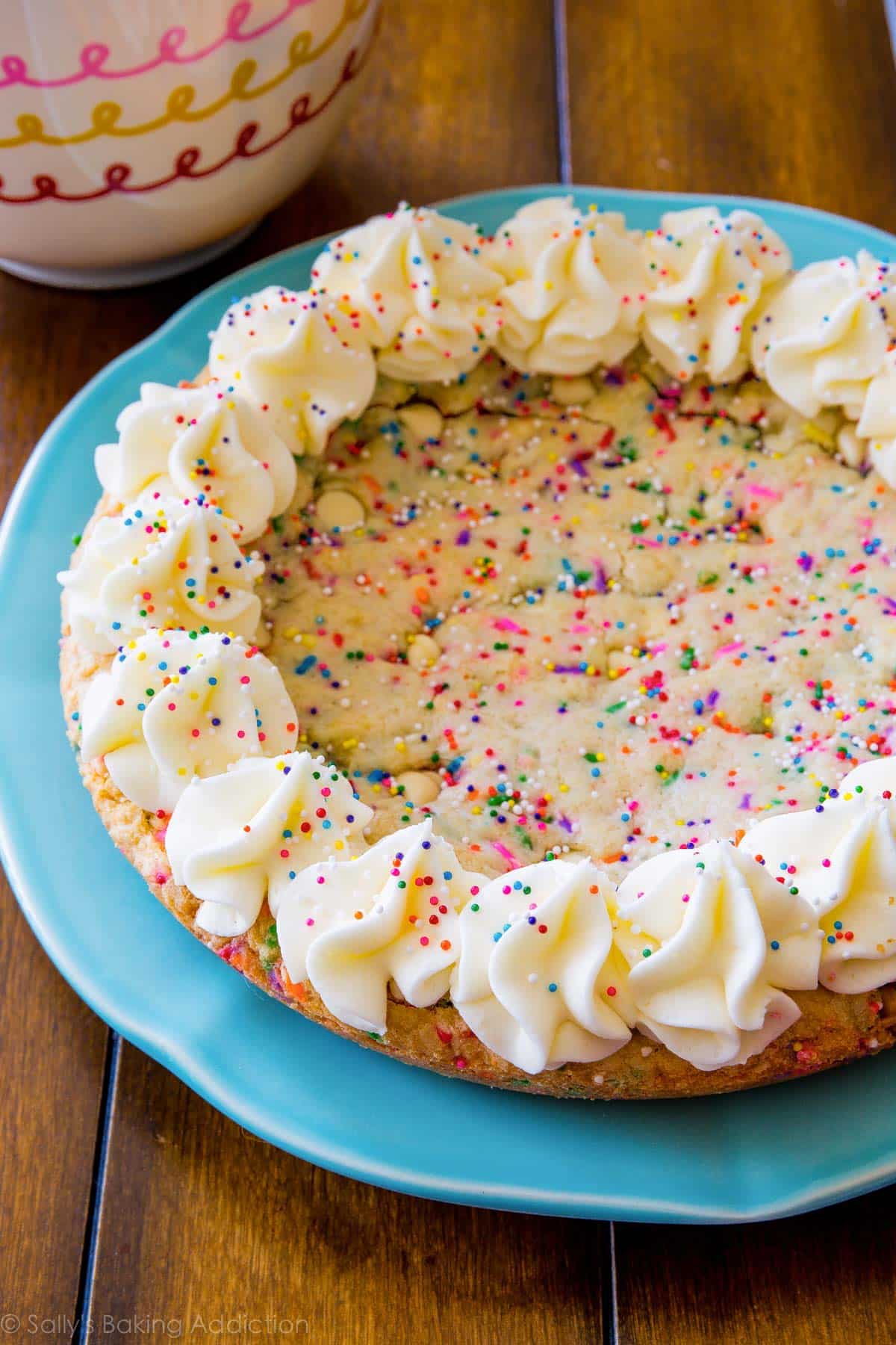 funfetti sugar cookie cake with piped frosting decorations and sprinkles on a blue plate