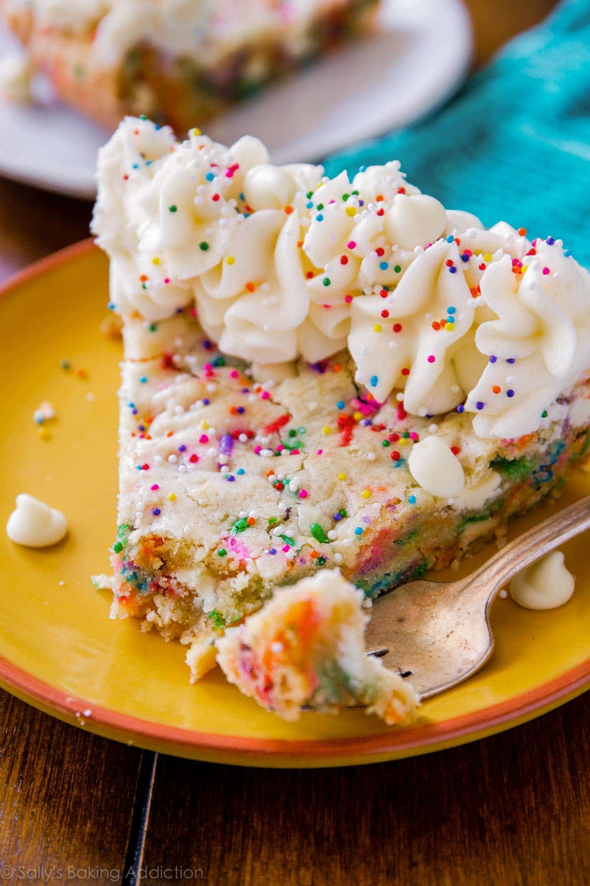 slice of funfetti sugar cookie cake on a yellow plate with a fork