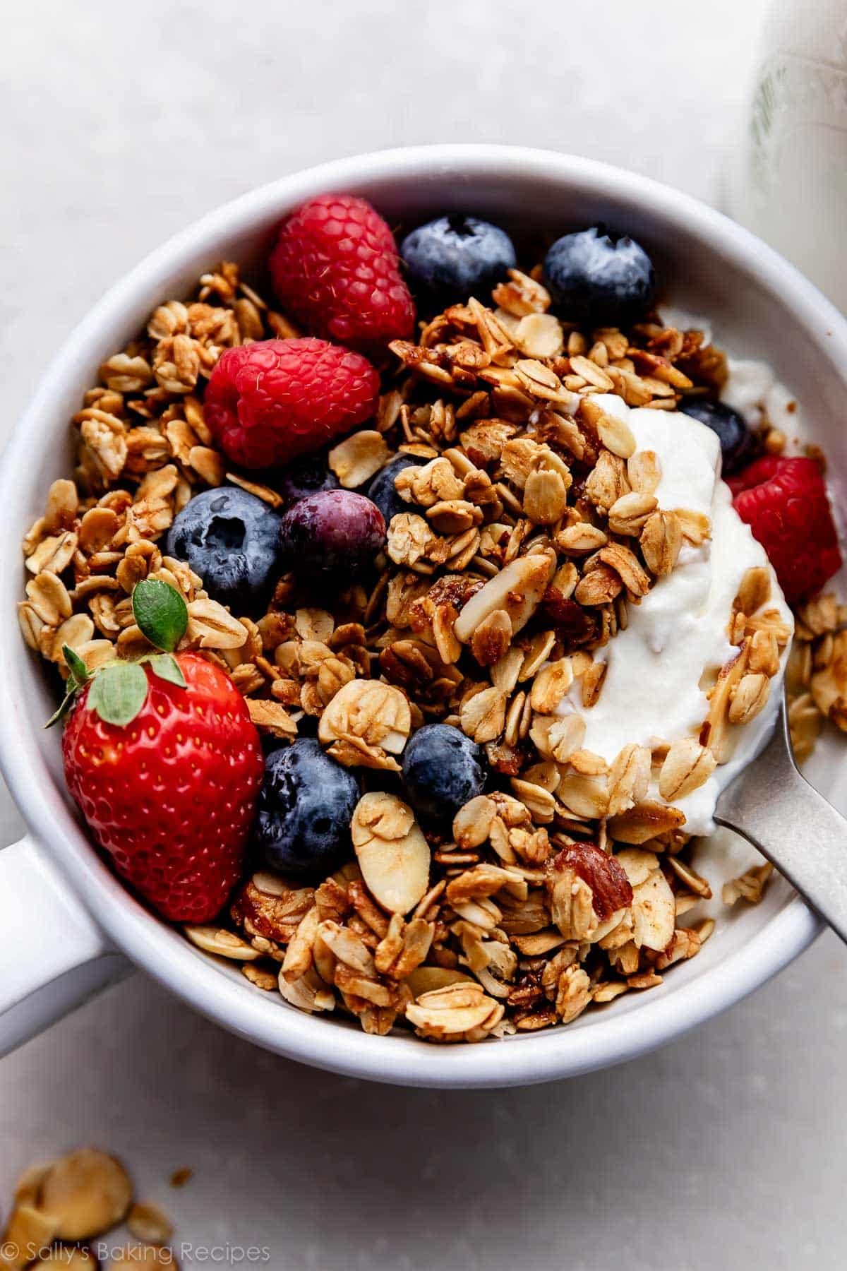 vanilla almond granola in white bowl with fresh berries and spoonful of yogurt.