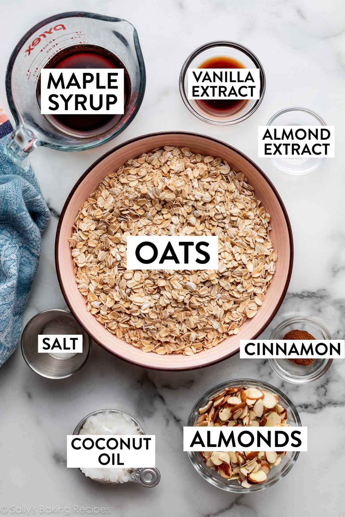 ingredients pictured in bowls including oats, maple syrup, vanilla extract, almonds, and coconut oil.