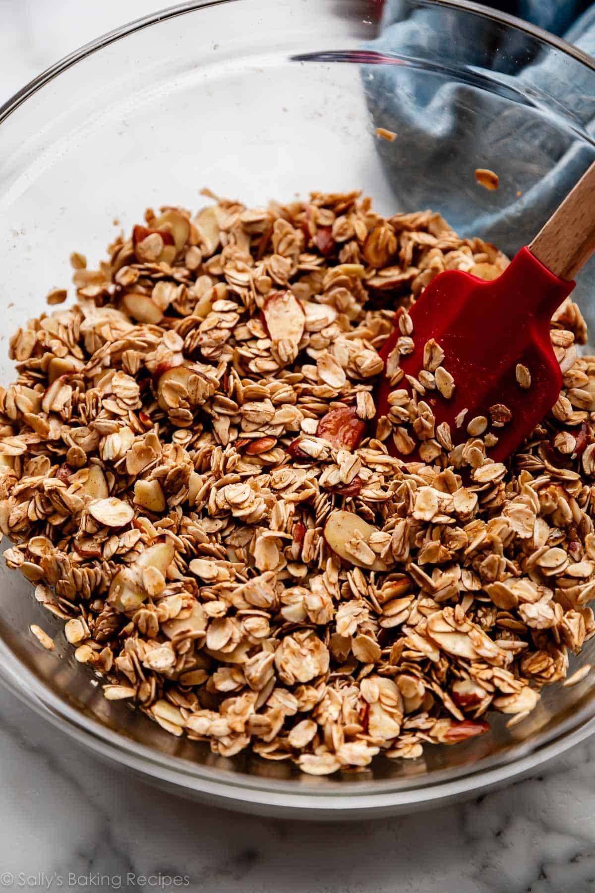 wet granola mixture mixed together in glass bowl with red spatula.