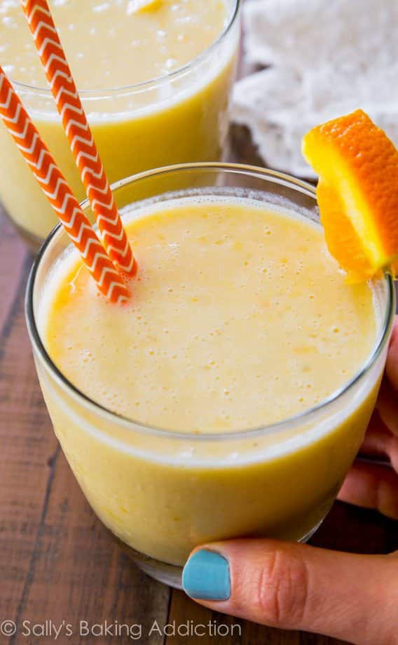 hand holding a creamsicle smoothie in a glass with straws